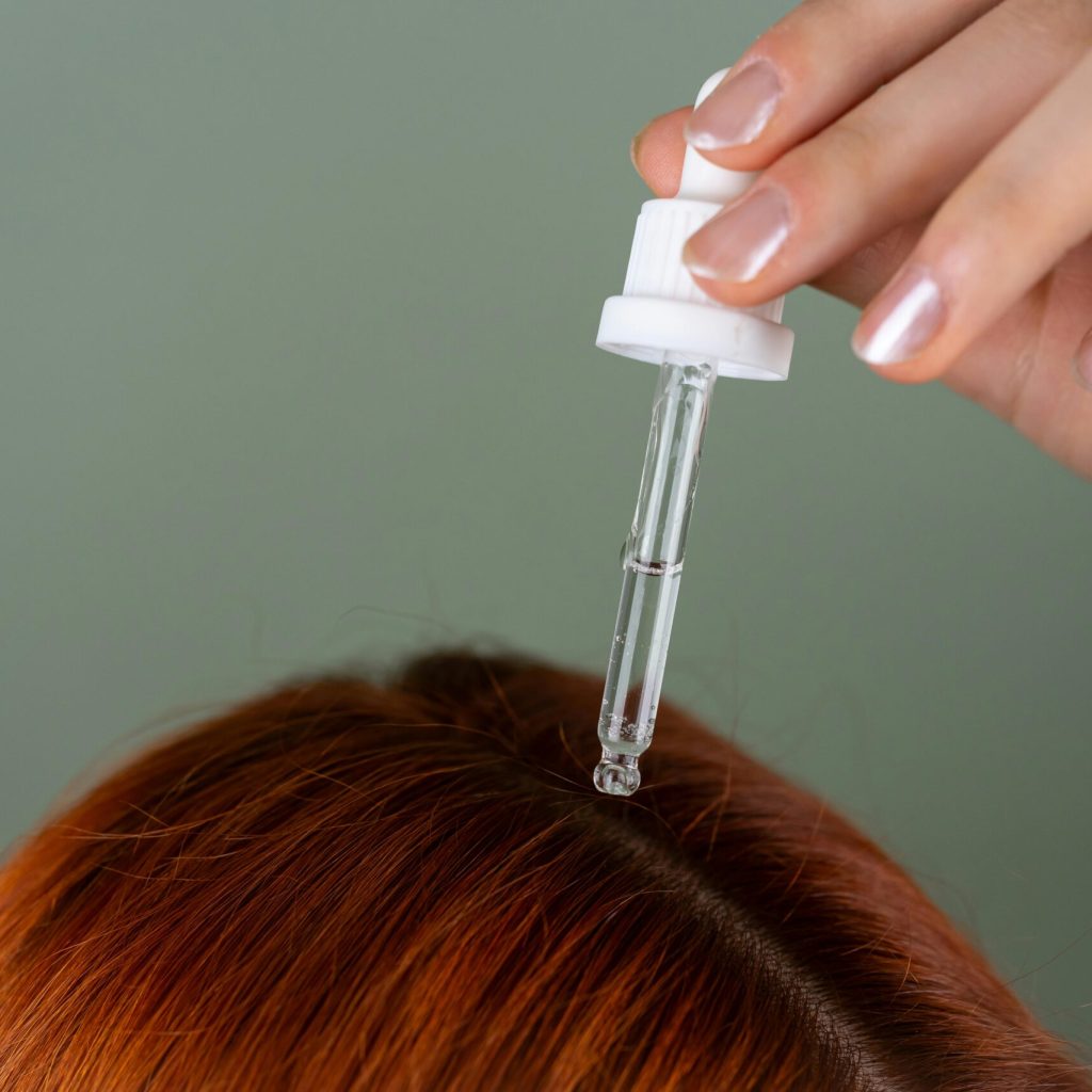 Close-up of applying serum to roots with a precision dropper on red hair, showcasing hair care routine.