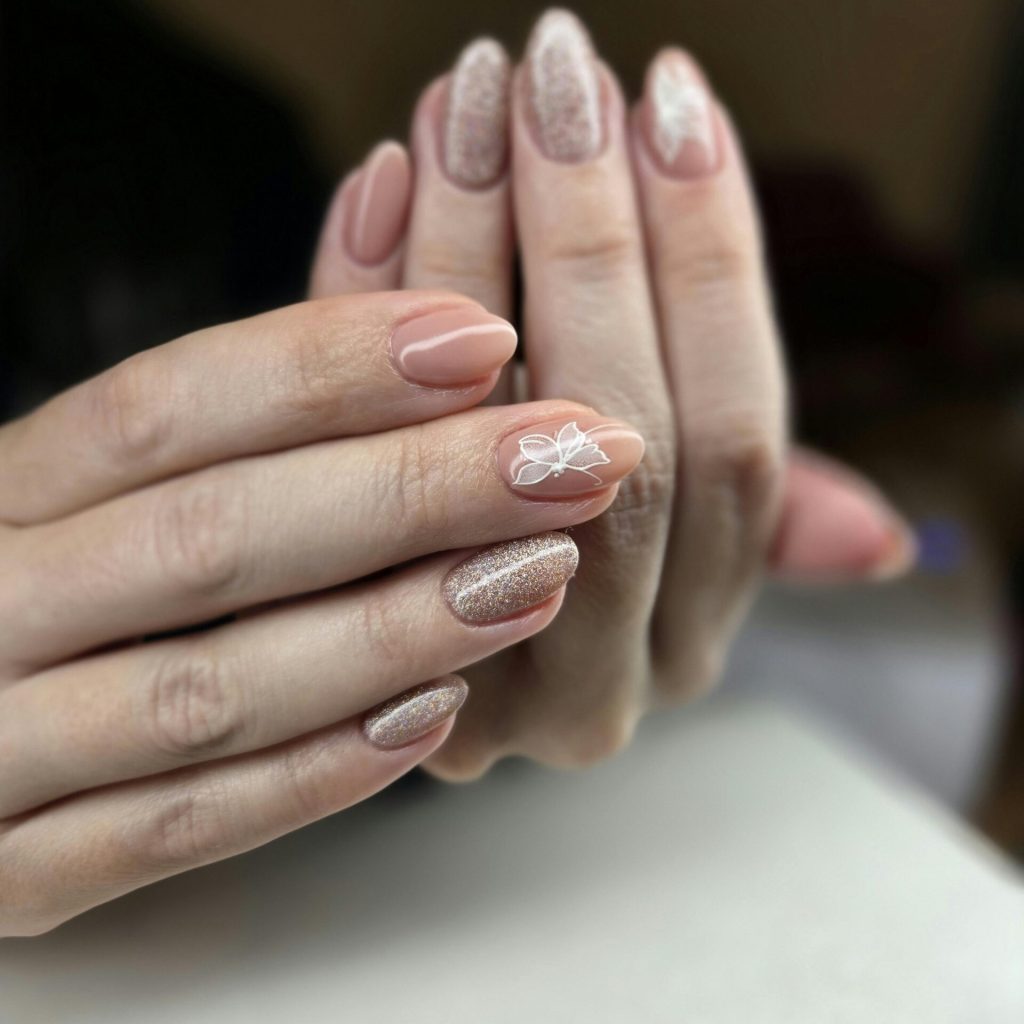 Close-up of elegant nude and glitter manicure with floral design on nails.