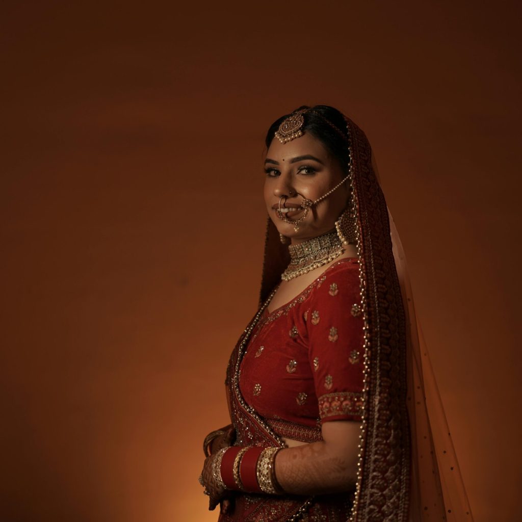 A beautiful Indian bride in traditional red lehenga and jewelry, posing gracefully.