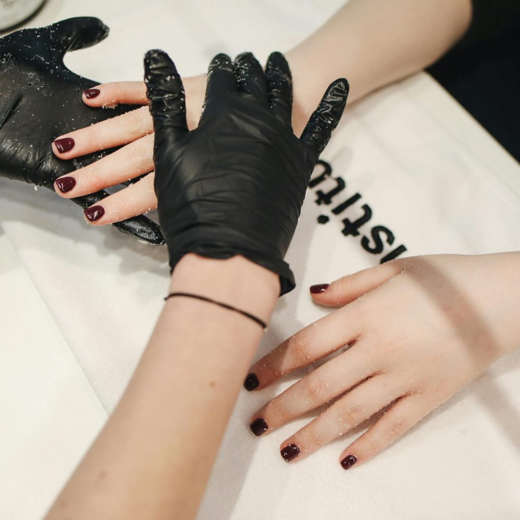 Close-up of a manicure session with black gloves applying hand treatment in a salon setting.