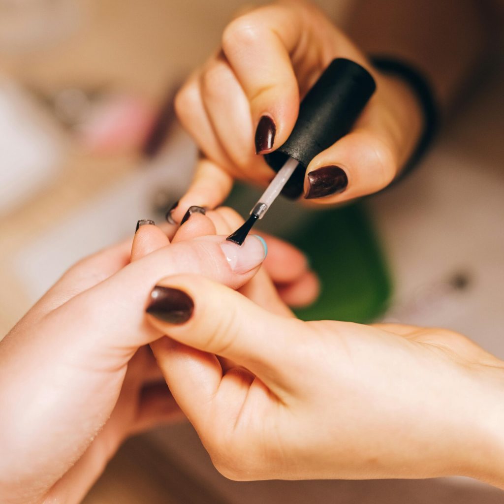 Close-up of a manicurist applying nail polish during a professional manicure session.