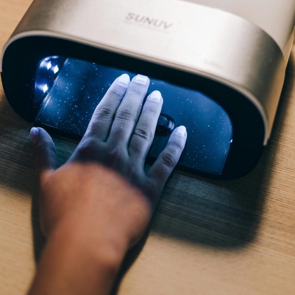 Hand receiving a gel manicure under a UV nail dryer, highlighting beauty care technology.