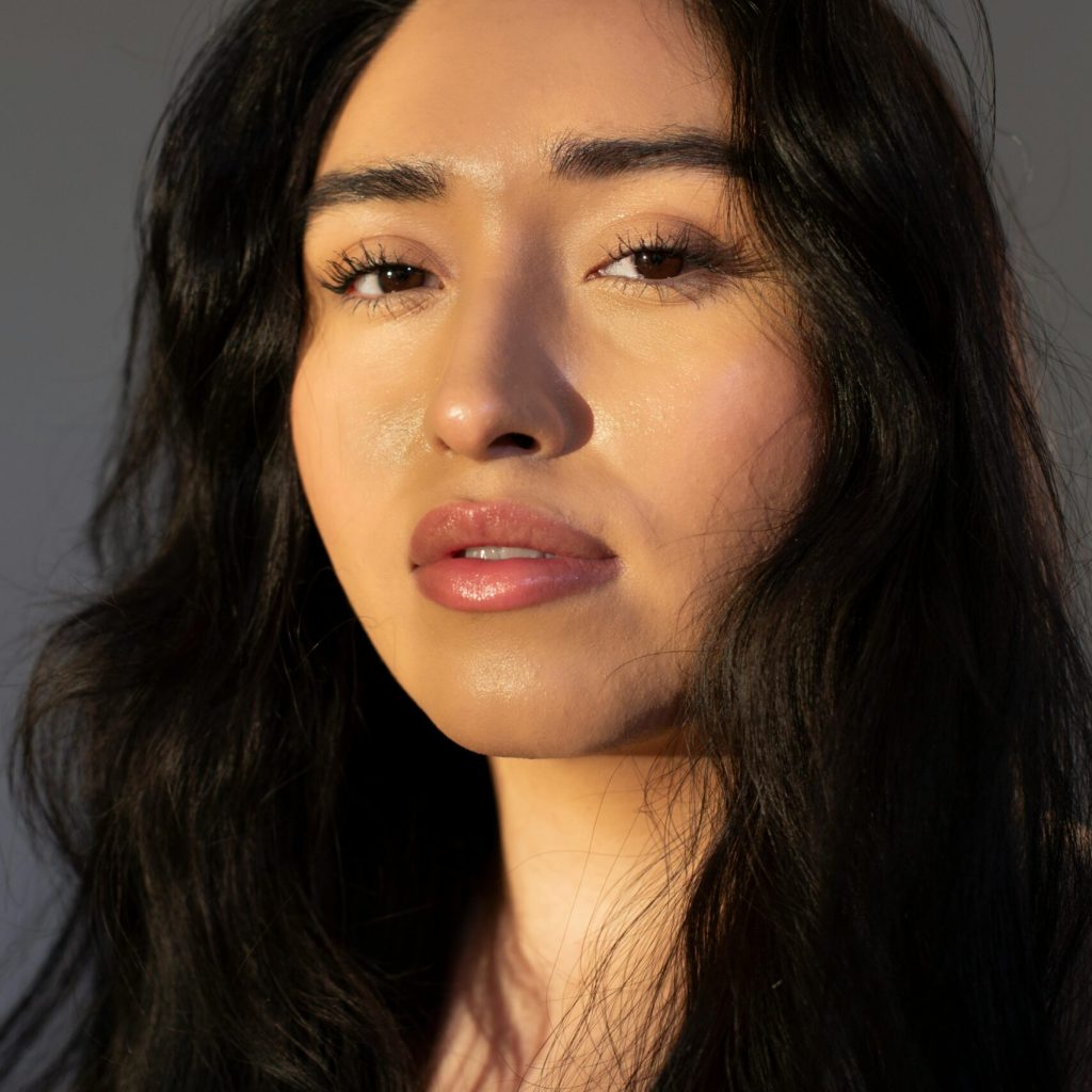 Young female with long dark hair looking at camera on gray background of studio